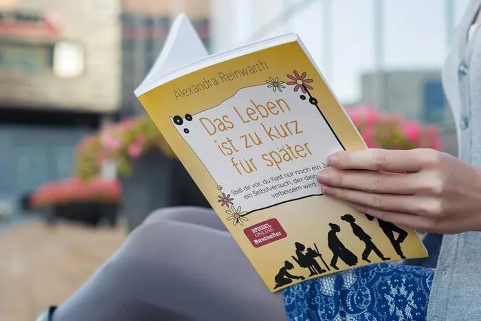 Eine Frau sitzt mit dem aufgeschlagenen Buch "Das Leben ist zu kurz für später"